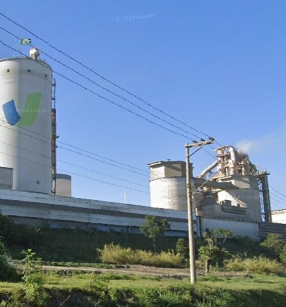 Industrial plant with a tall white silo and processing buildings under a clear blue sky