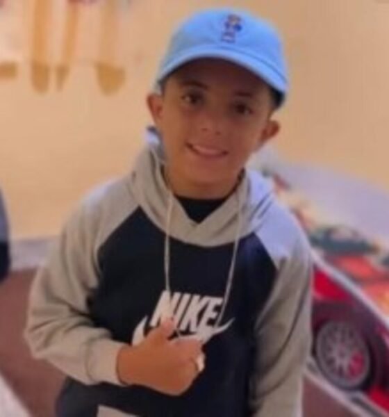 Smiling young boy wearing a blue cap and a gray black Nike hoodie looking at the camera indoors