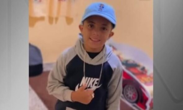 Smiling young boy wearing a blue cap and a gray black Nike hoodie looking at the camera indoors