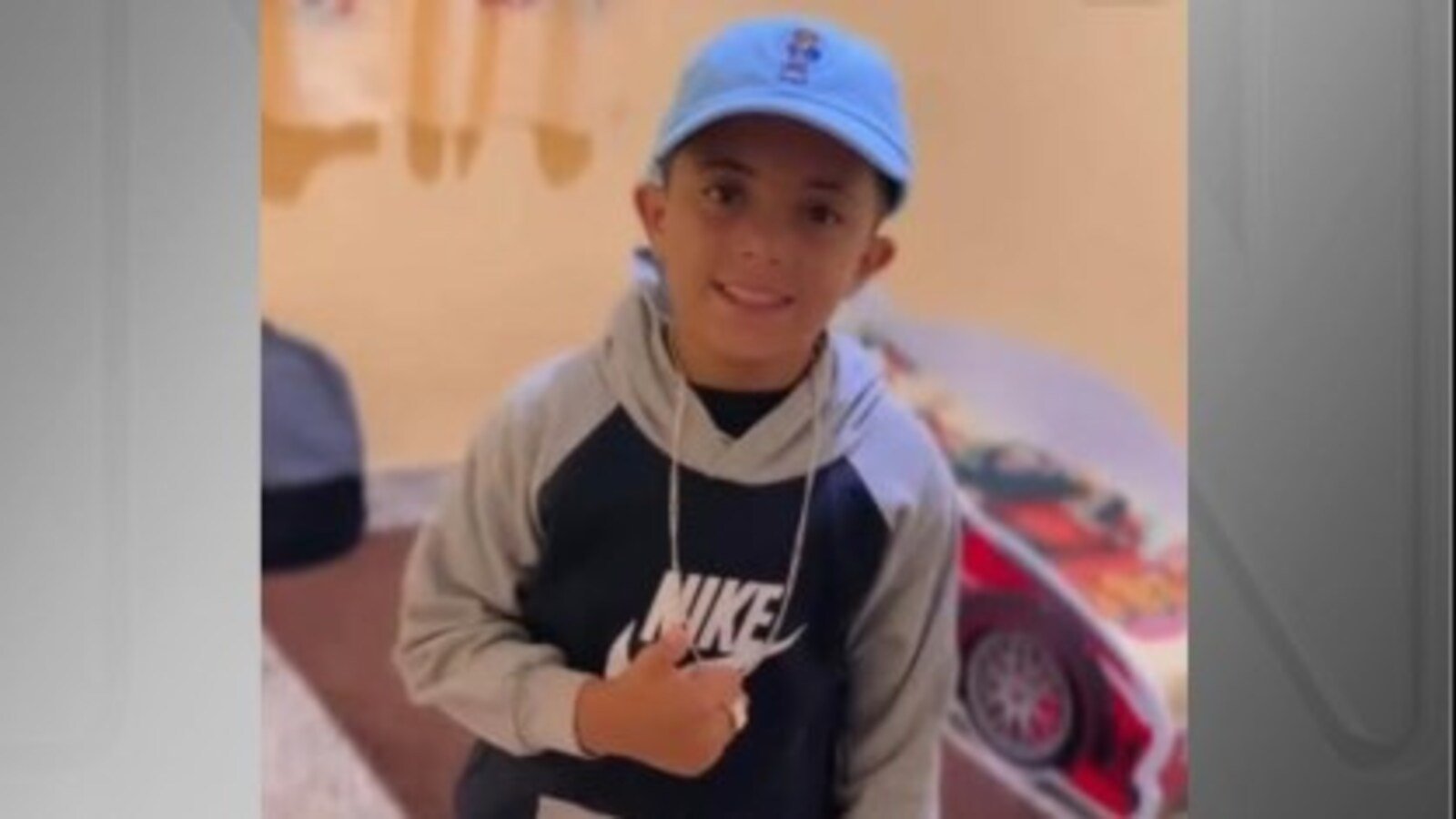 Smiling young boy wearing a blue cap and a gray black Nike hoodie looking at the camera indoors