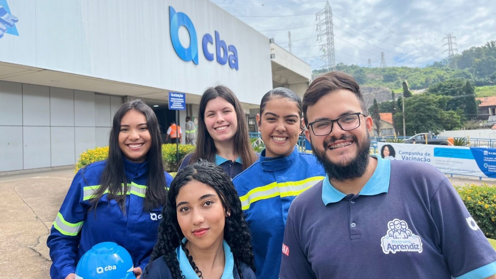 Group of five volunteers in blue uniforms pose outside a building with a CBA sign smiling for the photo during a vaccination campaign
