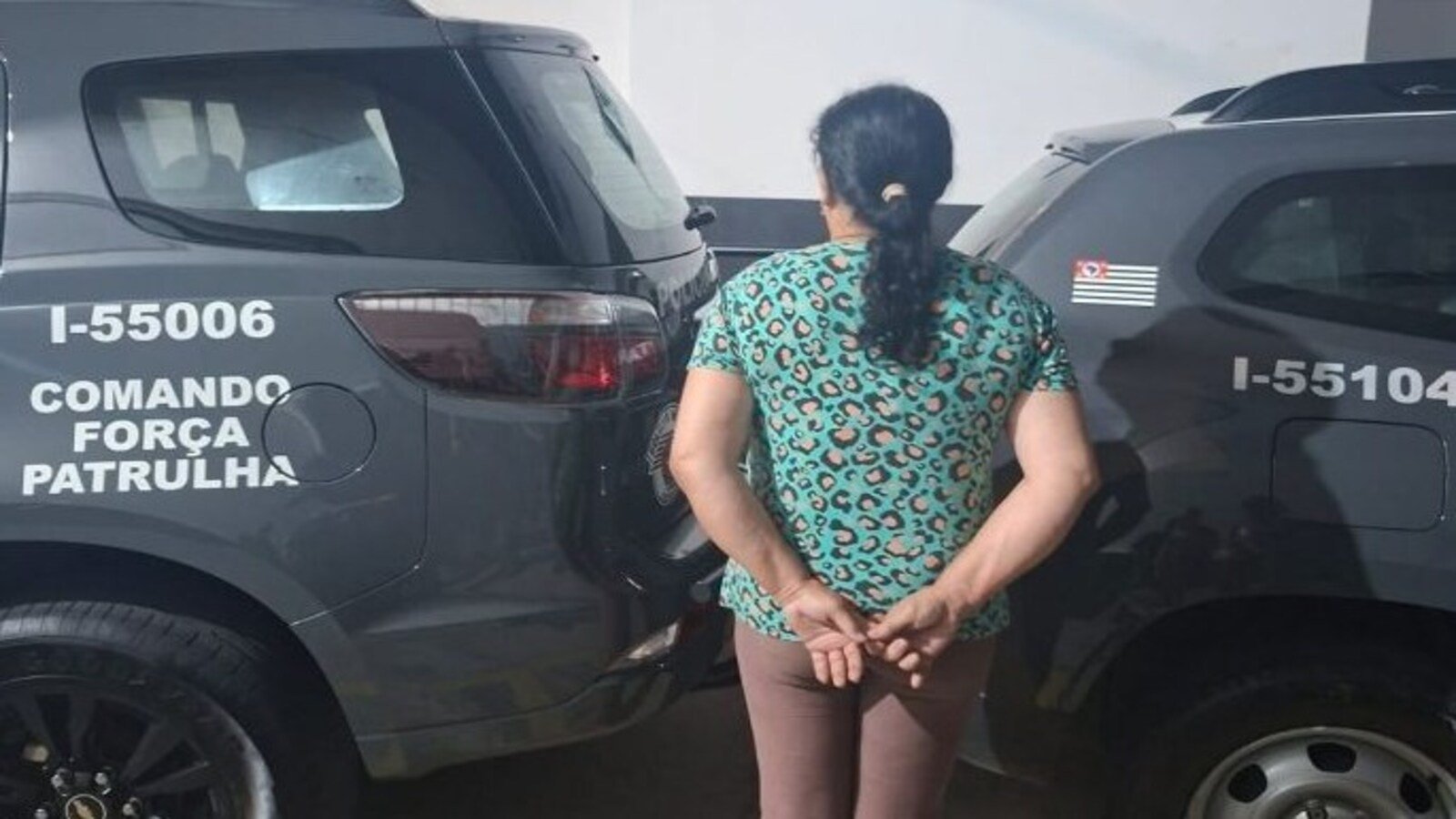 Woman in a teal leopard print shirt stands with hands behind her back between two dark gray patrol SUVs