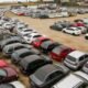 Aerial view of a vast dirt parking lot filled with rows of cars in various colors and sizes stretching into the distance