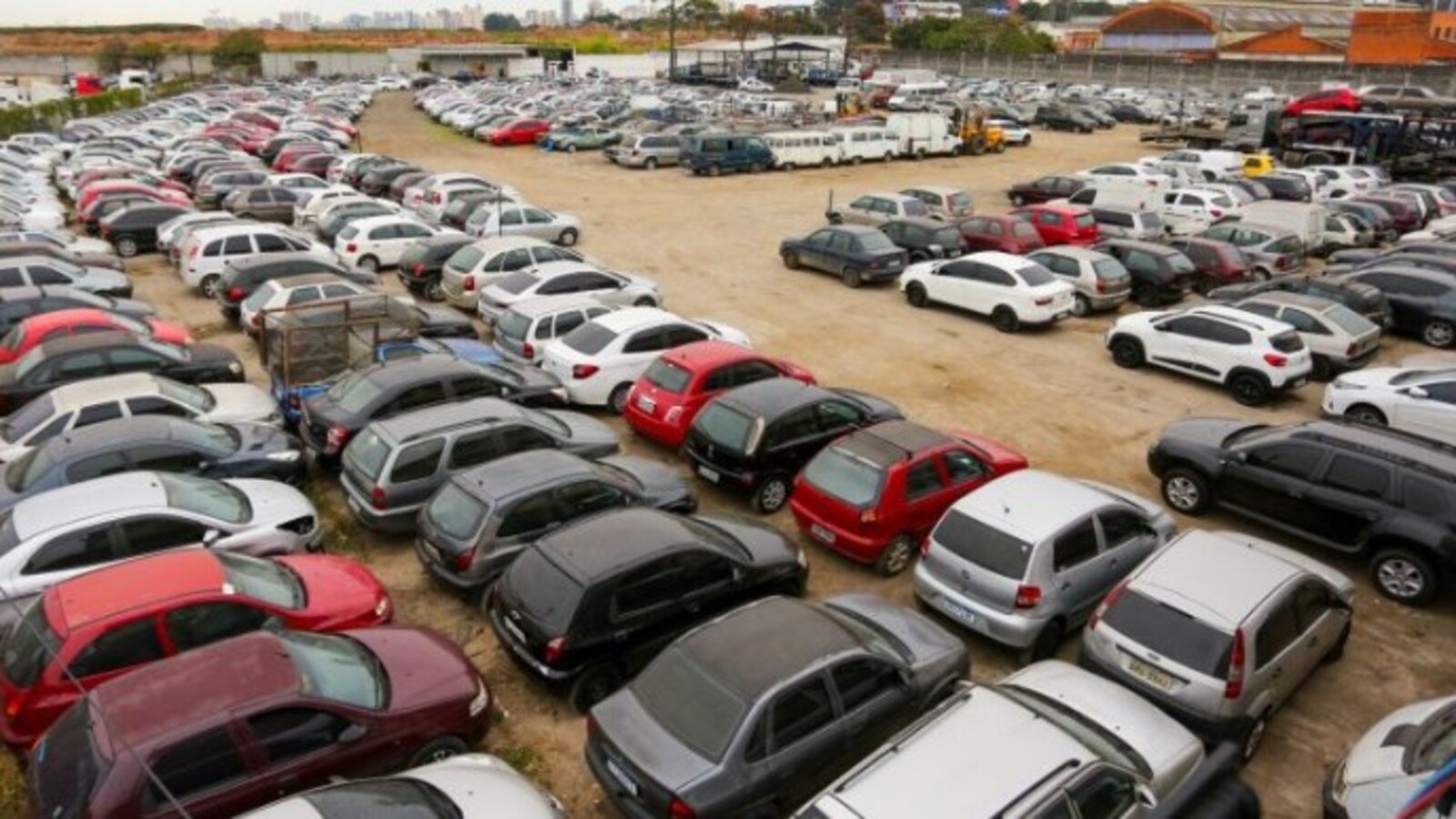 Aerial view of a vast dirt parking lot filled with rows of cars in various colors and sizes stretching into the distance