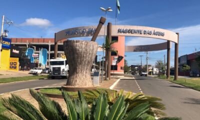Entrance arch to Pilar do Sul with a large stone pedestal sculpture in a circular planter and palm plants in the foreground cars on the street behind