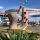 Entrance arch to Pilar do Sul with a large stone pedestal sculpture in a circular planter and palm plants in the foreground cars on the street behind