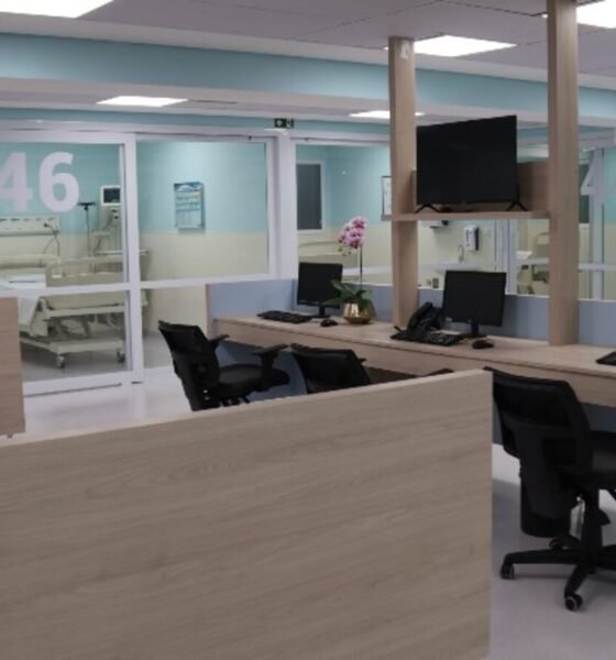 Hospital reception desk with multiple workstations and computer monitors in a bright modern ward area glass doors labeled  and  in the background