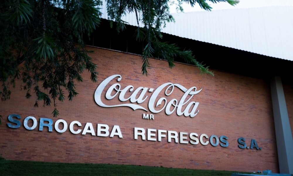 Brick wall with a large Coca Cola logo and the words SOROCABA REFRESCOS SA under it with overhanging tree branches