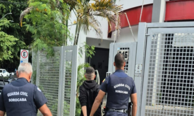 Two Guarda Civil Sorocaba officers escort a man toward a gated entrance