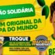 Jovem brasileiro com camiseta amarela e rosto pintado vibra ao lado de uma caixa de alimentos para uma ação solidária da Copa do Mundo