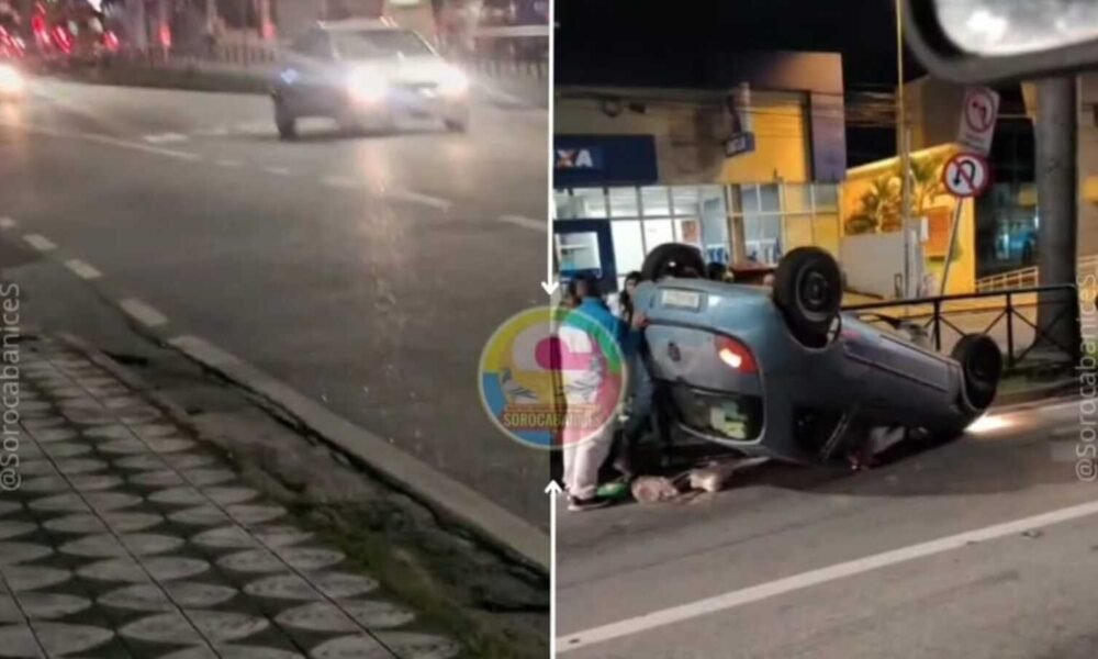 Nighttime scene of a blue car upside down on a city street while people assist at the roadside