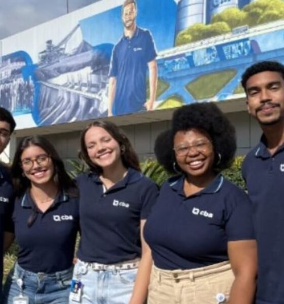 Five smiling young adults in navy polo shirts with a company logo stand together outdoors in front of a mural