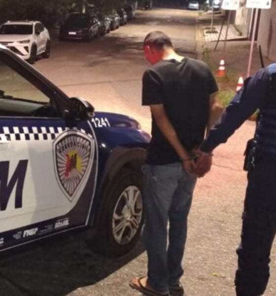 Uniformed officer detains a man in a black tshirt and jeans handcuffing him beside a white and blue GCM police SUV on a dim city street at night