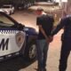 Uniformed officer detains a man in a black tshirt and jeans handcuffing him beside a white and blue GCM police SUV on a dim city street at night