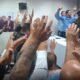 Crowd with raised hands facing a panel at a meeting blue banner visible in the background