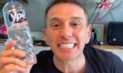 Smiling man in a black shirt holds up a clear plastic water bottle toward the camera blue label visible on the bottle