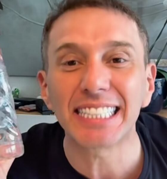 Smiling man in a black shirt holds up a clear plastic water bottle toward the camera blue label visible on the bottle