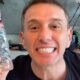 Smiling man in a black shirt holds up a clear plastic water bottle toward the camera blue label visible on the bottle