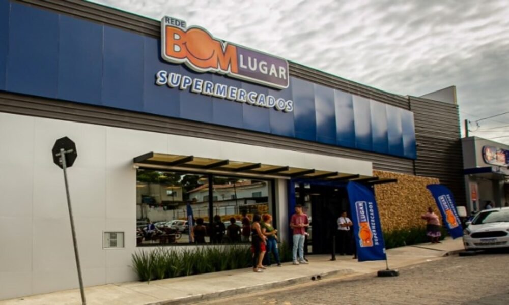 Exterior of Bom Lugar Supermercados storefront with blue panels and glass entrance, people standing outside under an awning.