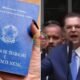Blue Brazilian work and social security booklet held up with Carteira de Trabalho e Previdência Social visible on the cover Left side shows the document right side shows a man in a suit speaking into a microphone at a podium