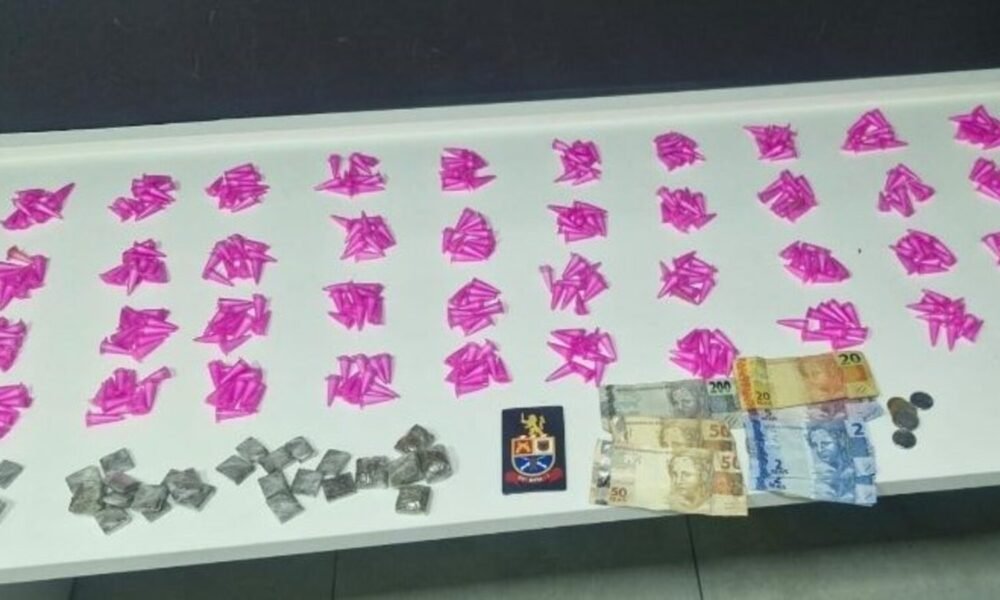 Row of bright pink paper shapes spread on a table with stacks of banknotes, coins, and a small emblem/crest nearby.