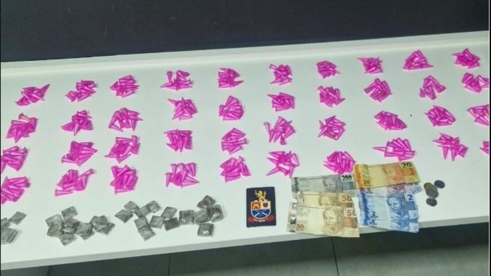 Row of bright pink paper shapes spread on a table with stacks of banknotes coins and a small emblemcrest nearby