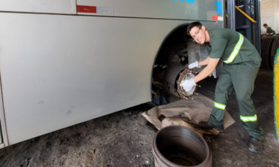 Male mechanic in green coveralls and gloves installing or inspecting a bus wheel brake rotor beside an open wheel in a garage workshop