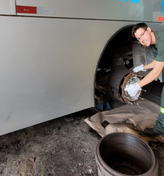 Male mechanic in green coveralls and gloves installing or inspecting a bus wheel brake rotor beside an open wheel in a garage workshop