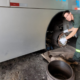 Male mechanic in green coveralls and gloves installing or inspecting a bus wheel brake rotor beside an open wheel in a garage workshop