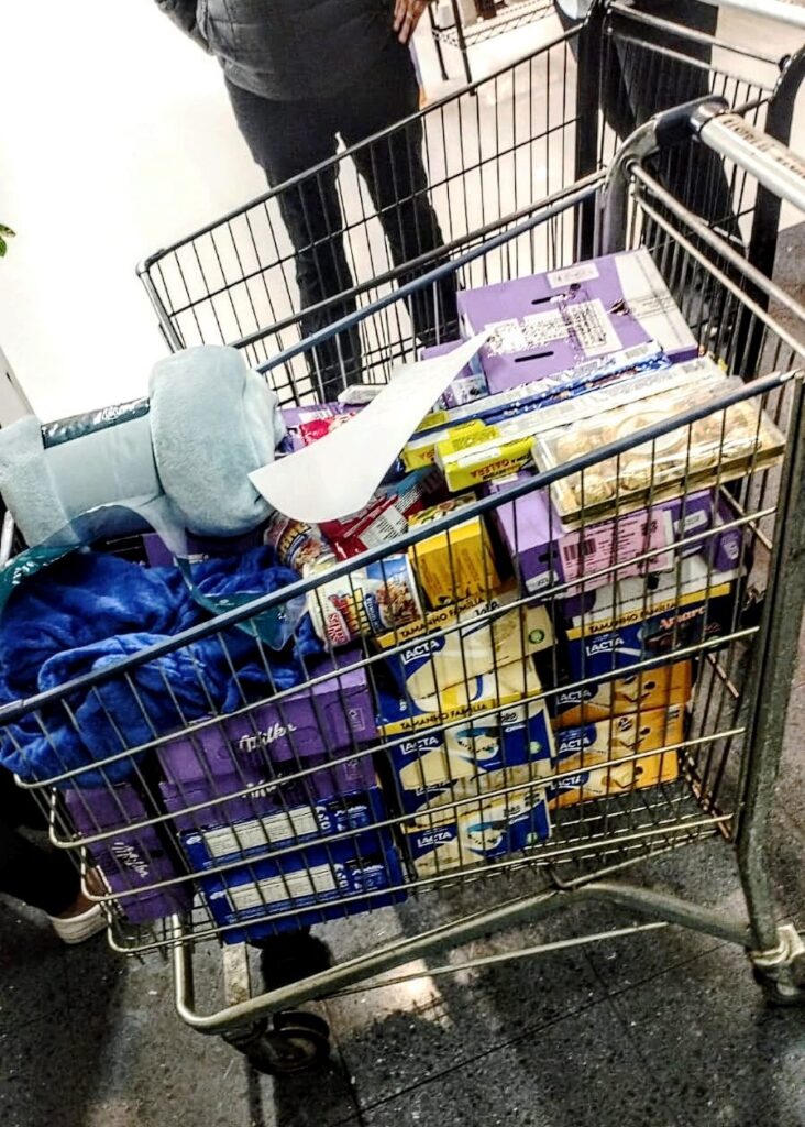 2 sorocabanices Shopping cart overflowing with purple and yellow chocolate boxes and papers in a grocery store