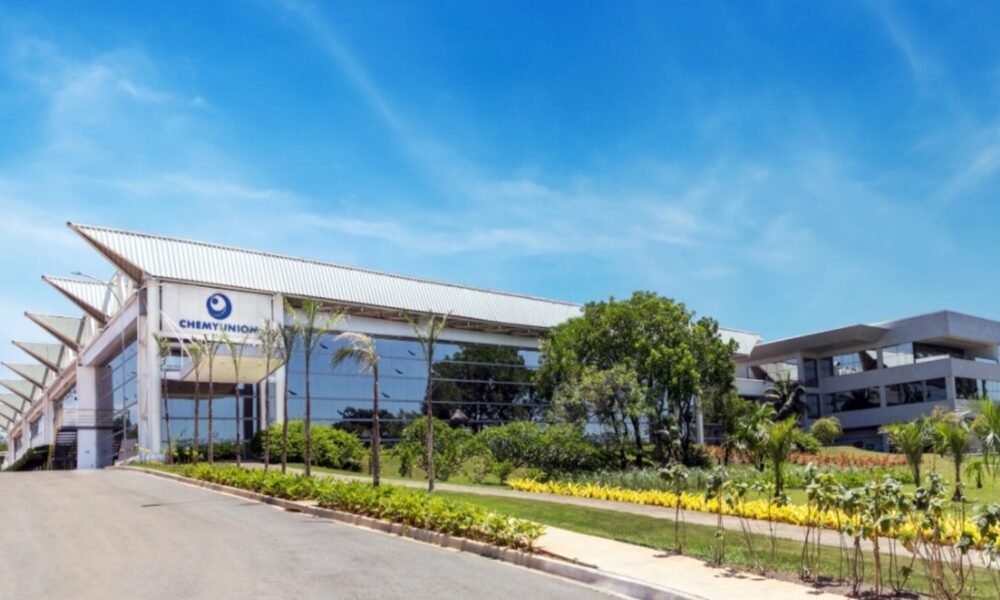 Modern glass-front corporate building with ChemyUnion sign, surrounded by palm trees on a sunny day.