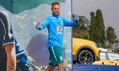Brazilian footballer in blue training kit giving thumbs up on a sports stagefield smiling at the camera