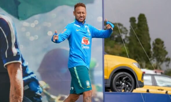 Brazilian footballer in blue training kit giving thumbs up on a sports stagefield smiling at the camera