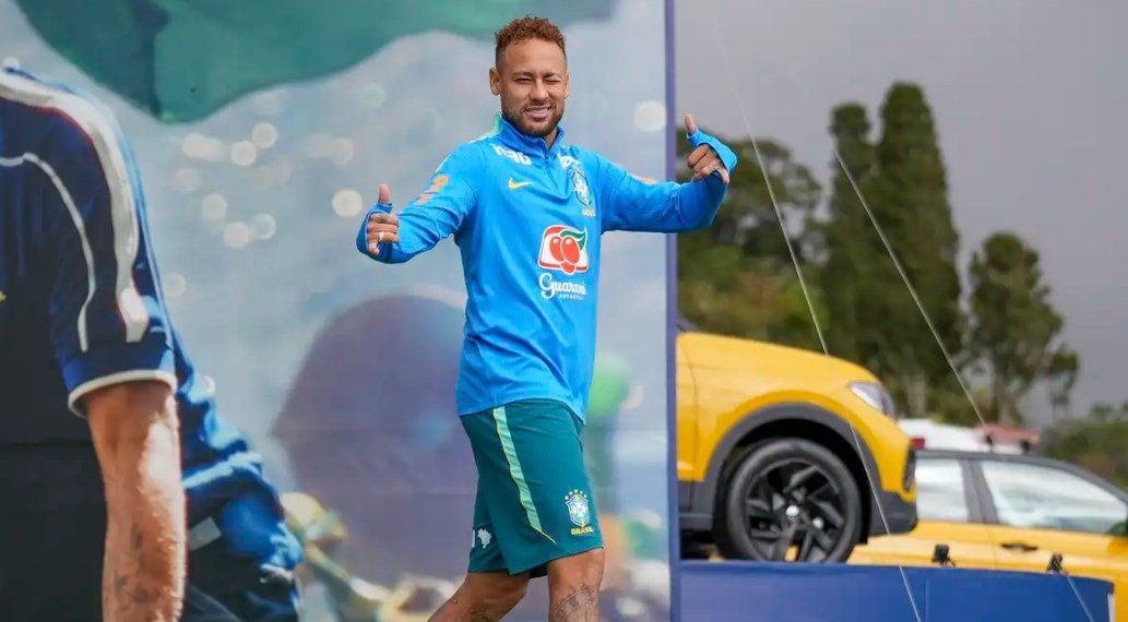 Brazilian footballer in blue training kit giving thumbs up on a sports stagefield smiling at the camera