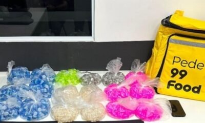 Colorful bags of small snacks in plastic wrap arranged on a white counter beside a yellow delivery bag labeled Pede  Food and a phone