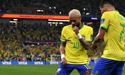 Two Brazil players in yellow jerseys celebrate on the pitch as a full stadium looks on