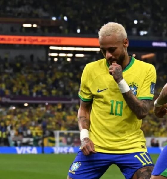 Two Brazil players in yellow jerseys celebrate on the pitch as a full stadium looks on