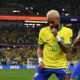 Two Brazil players in yellow jerseys celebrate on the pitch as a full stadium looks on