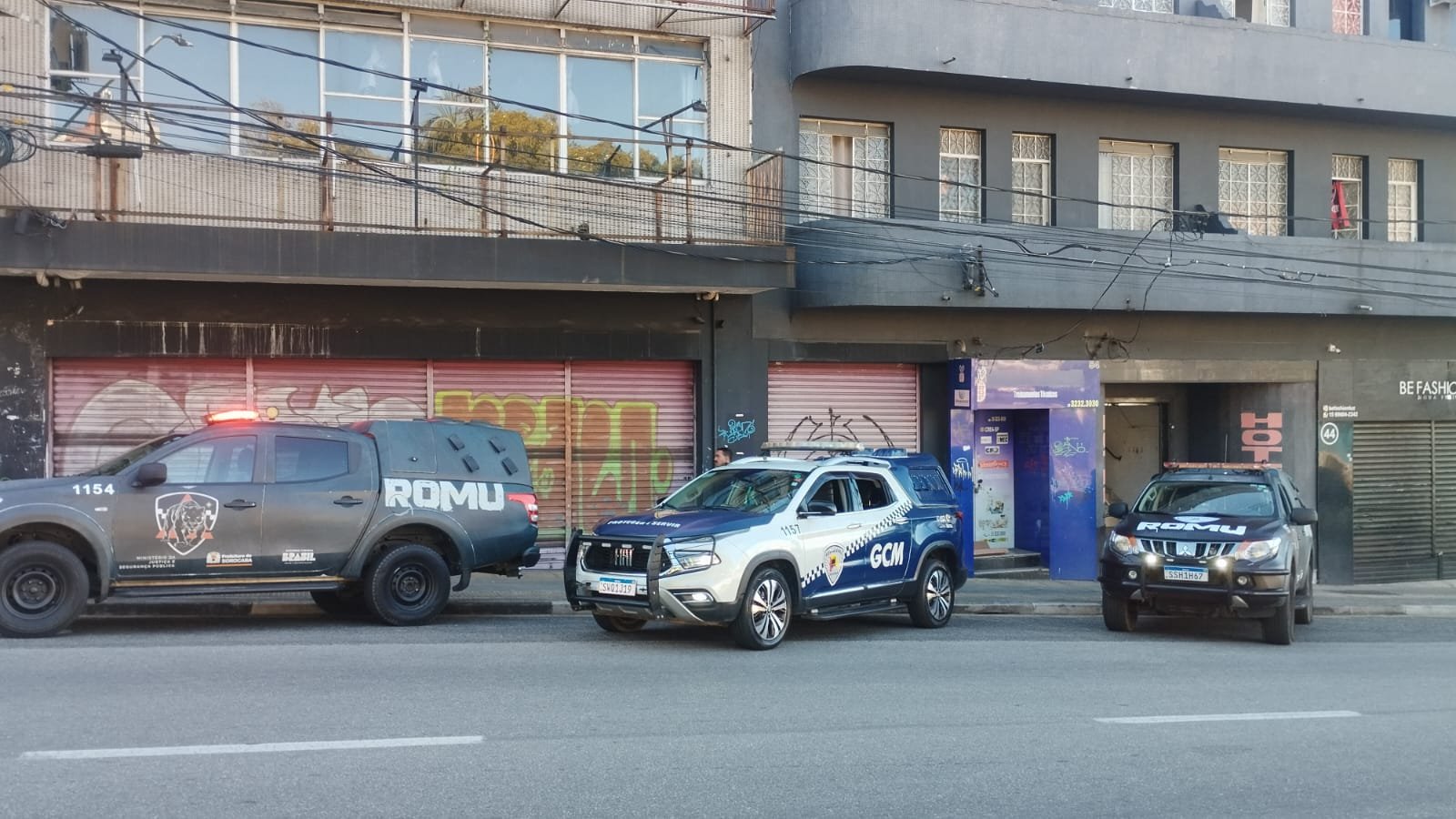 Three police vehicles parked along a city street in front of graffiti covered storefronts left a gray ROMU pickup center a white and blue GCM SUV right a dark ROMU SUV