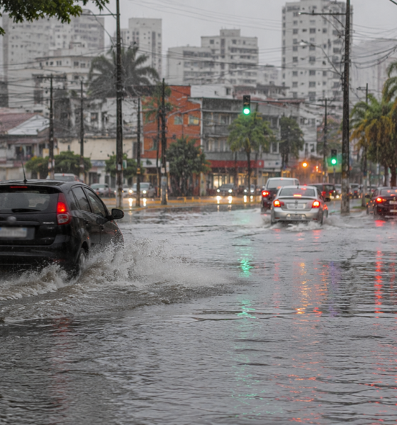 Urban street heavily flooded with cars driving through puddles reflections of traffic lights shimmer on the water as rain pours down the cityscape at dusk