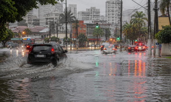Urban street heavily flooded with cars driving through puddles reflections of traffic lights shimmer on the water as rain pours down the cityscape at dusk