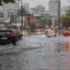 Urban street heavily flooded with cars driving through puddles reflections of traffic lights shimmer on the water as rain pours down the cityscape at dusk