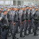 Line of uniformed officers standing at attention in a parade formation in gray uniforms with patches on sleeves