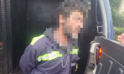 Man wearing a dark jacket with neon-reflective stripes leaning into an open van, a hand near the tailgate edge.
