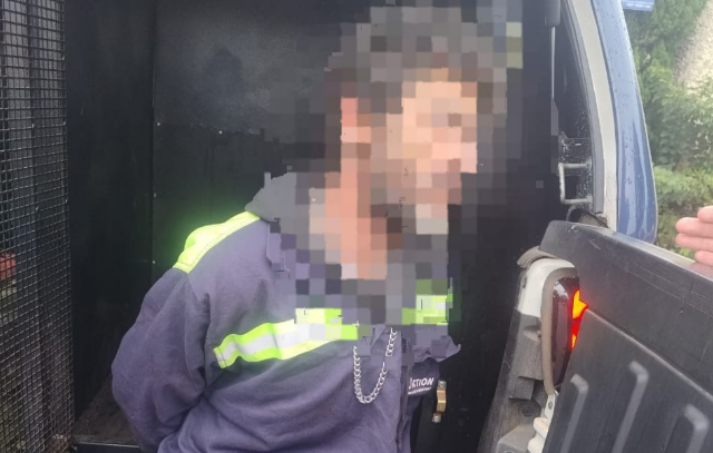Man wearing a dark jacket with neon reflective stripes leaning into an open van a hand near the tailgate edge