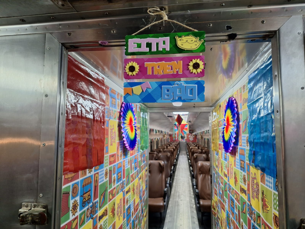 Inside a festively decorated bus or tram with bright patterned walls brown seats and a three piece hanging sign from the ceiling