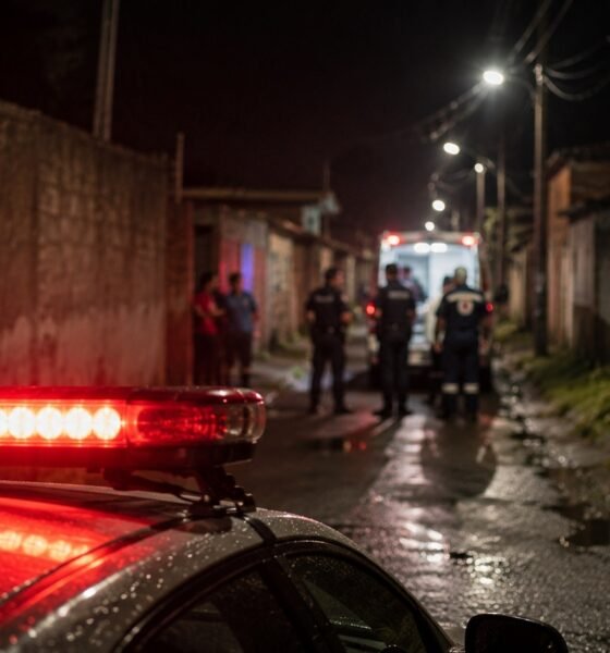 Nighttime alley scene with police and medics near an ambulance red emergency lights reflect on the wet street in the foreground
