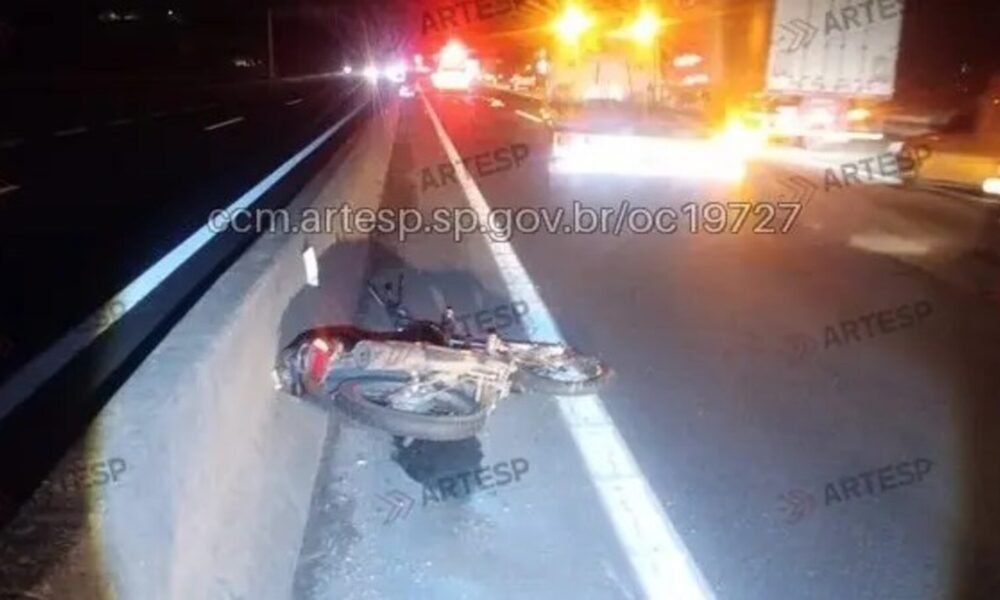 Motorcycle crash on highway at night lying on its side against a concrete barrier with emergency lights in the distance