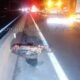 Motorcycle crash on highway at night lying on its side against a concrete barrier with emergency lights in the distance