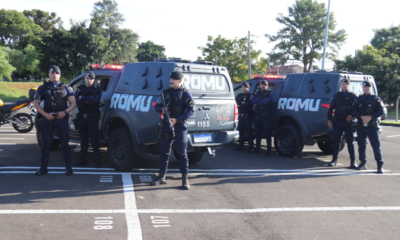 Group of tactical police officers standing in front of two large armored vans marked ROMU in a parking lot.